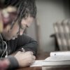 man writing on paper near book on table