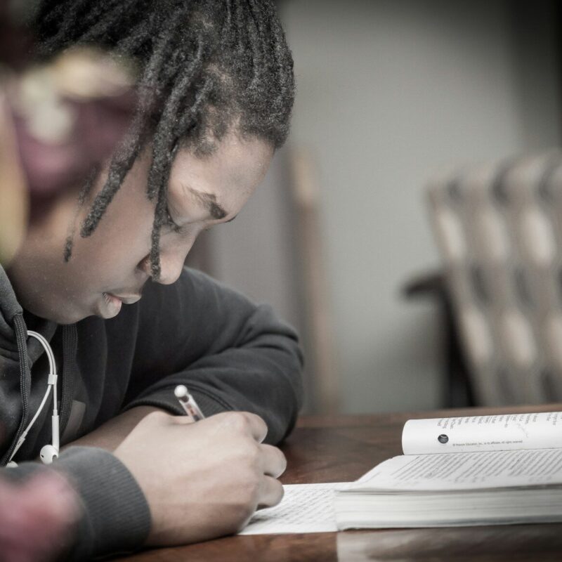 man writing on paper near book on table